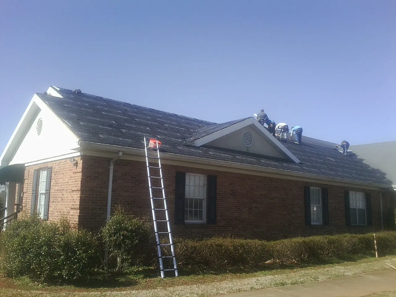 Crew tearing shingles off a brick ranch roof with a ladder set — Metal Roof Repair work by our crew in Bamberg