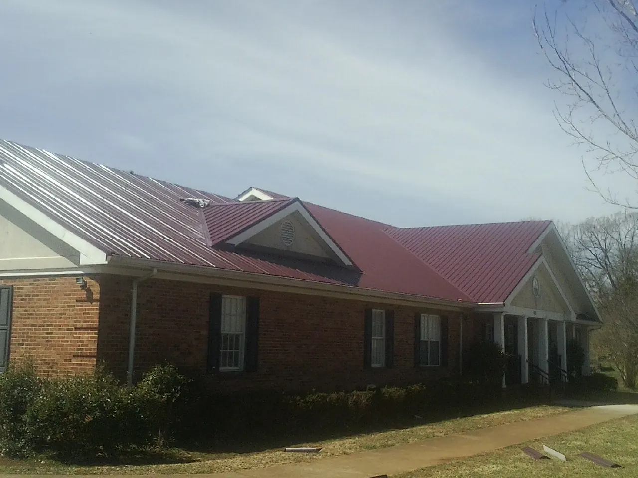 Red metal roof with gabled entries on a long brick building, from a Hail Damage Roof Repair job in Bamberg
