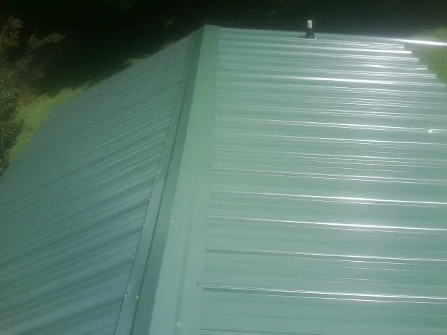 New green metal panels meeting at the ridge of a roof — Flat Roof Repair work by our crew in Bamberg