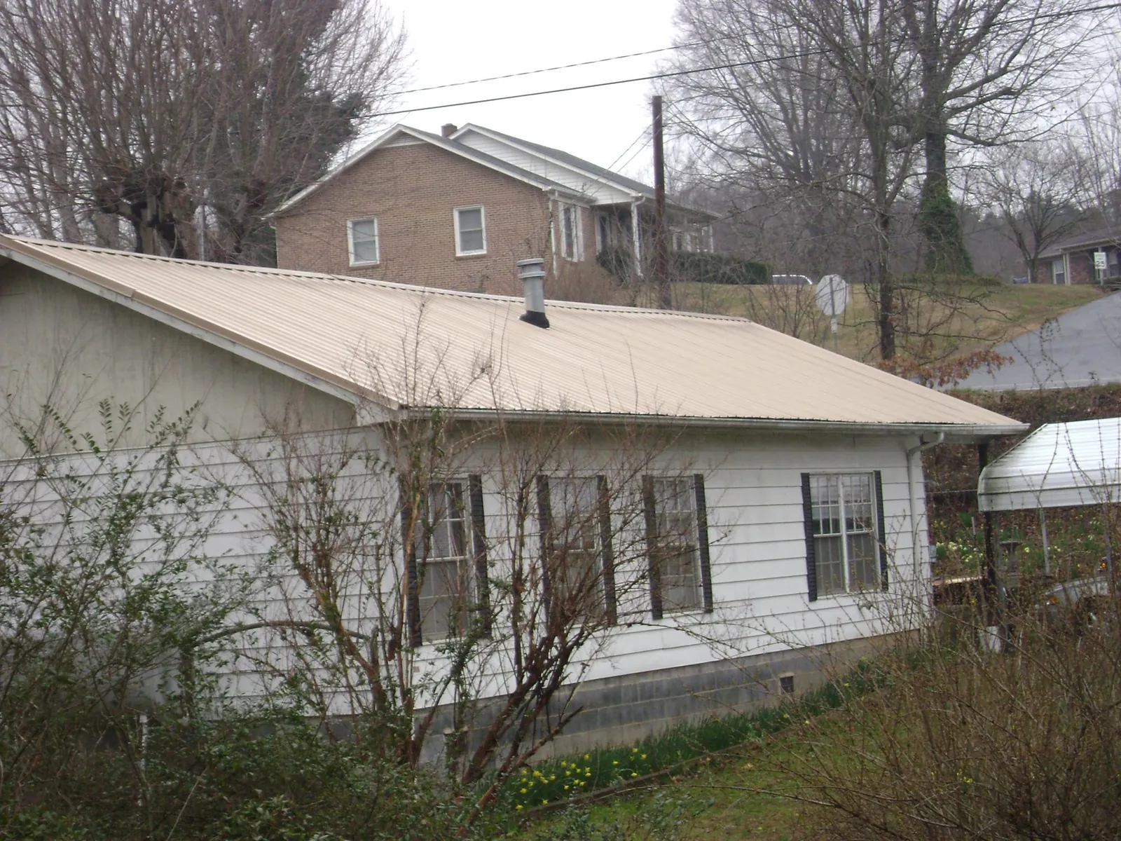 Tan metal roof on a white sided house set into a hillside — Commercial Roofing by Roofing Brothers in Bamberg